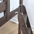 Close-up of dark-stained wooden bunk bed ladder with metal brackets and gray mattress cushion in a modern bedroom