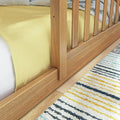 Close-up of natural oak wooden slatted bed frame footboard with yellow bedding, white mattress and striped area rug on light hardwood floor — modern bedroom furniture detail