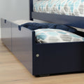 Under-bed storage trundle drawer in navy blue pulled out beneath a bed revealing patterned teal and gray pillows and a folded navy blanket on a hardwood floor