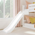 White wooden bunk bed with slide, blush pink and yellow pillows, pale curtains and window with tree view in a bright modern kids' bedroom