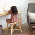 Child writing at wooden desk on rattan stool with notebook and pastel rainbow lamp in cozy home study