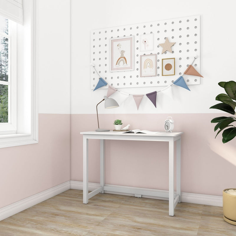 Minimal white writing desk against a pastel pink half-wall nursery with pegboard wall art, rainbow prints, bunting, lamp, succulent and alarm clock