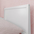 White wooden headboard against pink scallop-pattern wallpaper with blush quilted bedding in a modern bedroom
