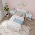 Pastel girls' bedroom with white twin bed, pink patterned wallpaper, pastel pillows and blue throw, white nightstands with geometric blue lamps, potted plant and rainbow wall art