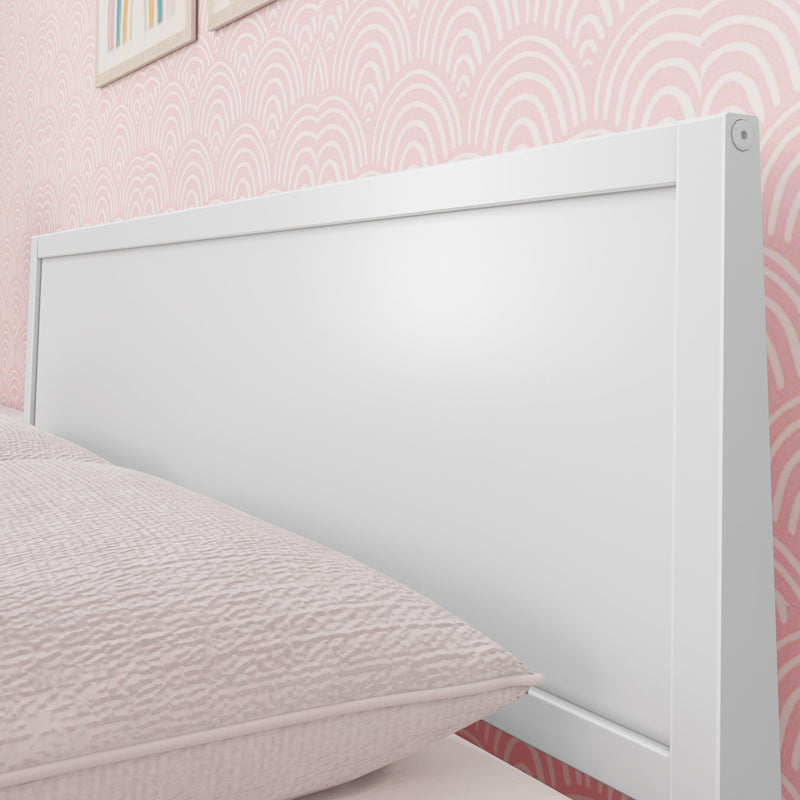Close-up of white wooden headboard with textured pink bedding and scallop-pattern pink wallpaper in girls' bedroom decor