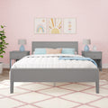 Girl's pastel bedroom interior with grey bedframe, white quilted bedding, pink scalloped wallpaper, three rainbow and sun prints above headboard, matching nightstands with blue lamps and nursery decor