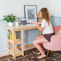 Girl studying at a light wood desk in a cozy home study nook with pink chair, potted plant, motivational "Don't Stop Until You're Proud" poster and patterned rug.
