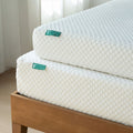 Stacked white 5-inch and 8-inch gel memory foam mattresses with quilted cover on wooden bed frame, close-up of corner and textured surface