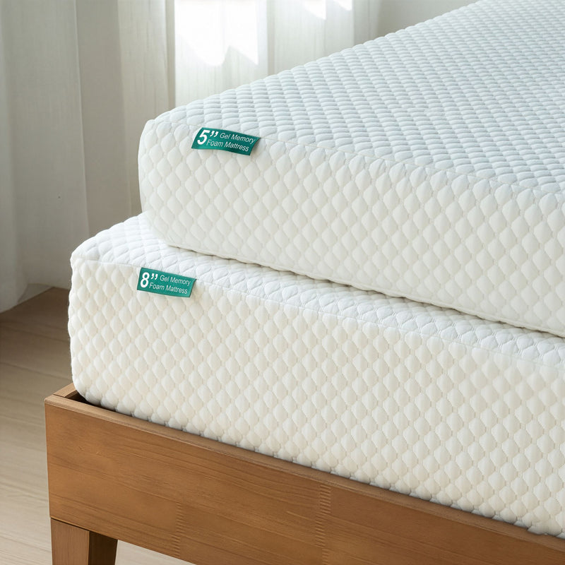 Stacked white 5-inch and 8-inch gel memory foam mattresses with quilted cover on wooden bed frame, close-up of corner and textured surface