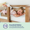 Smiling child on white mattress behind wooden bunk bed guardrail, illustrating low-profile bunk bed guardrail safety for kids