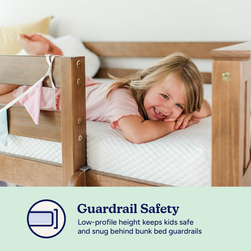 Bunk bed guardrail safety — smiling young child lying on a mattress behind a low-profile wooden guardrail, secure snug fit for kids