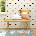 Stylish kids room nursery decor with pastel triangle wallpaper, wooden bench, cloud pillow, yellow-pink striped cushion, teal rug and pink cat slippers