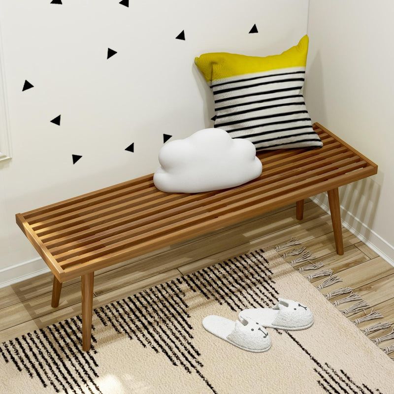 Minimalist room corner with wooden bench, decorative pillows, and cozy indoor slippers on a modern patterned rug.