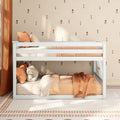 White wooden bunk bed in cozy kids bedroom with peach bedding, orange pillows, small floral beige wallpaper and plush teddy bear, nursery decor
