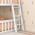 White wooden bunk bed ladder with peach bedding in a modern nursery featuring orange floral wallpaper and a striped rug