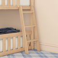 Wooden bunk bed ladder close-up with natural wood rails, striped mattress, navy throw blanket and blue plaid rug against a beige wall in a kids' bedroom
