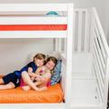 Two smiling children cuddling on an orange-quilted lower bunk of a white bunk bed in a bright modern kids' bedroom
