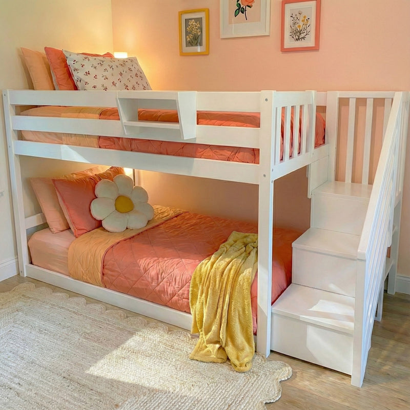 White wooden bunk bed with built-in stairs in pink and peach girls' bedroom, coral bedding, daisy cushion, yellow throw and floral wall art, kids room decor