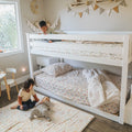Neutral boho kids' bedroom with white bunk bed, floral bedding, padded play mat and two children playing under pastel wall bunting