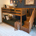 Solid wood twin-over-full bunk bed with built-in staircase storage, brown and striped bedding, and navy accent wall with framed art in a cozy bedroom
