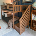 Solid wood twin-over-full bunk bed with staircase and built-in storage in cozy kids bedroom with navy accent wall, striped pillows and globe