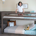 Smiling child standing on a rustic gray wooden bunk bed in a modern kids' bedroom with teal patterned bedding and playful decor