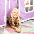 Smiling blonde girl in a purple play tent on a colorful geometric rug — indoor kids' playroom and sleepover fun