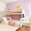White bunk bed with stairs in pastel pink kids bedroom, checkered quilt, unicorn plush, rainbow wall decor and 'FLOWER BABE' banner