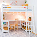 White loft bed with built-in desk and ladder, pastel rainbow wall art, string lights, wooden chair, potted plants and woven baskets in a bright modern kids' bedroom