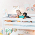 Smiling young girl with dachshund on a white bunk bed in a pastel kids' bedroom with rainbow wall art, cozy pillows, and playful kids bedroom decor