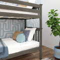 Grey wooden bunk bed in modern kids' bedroom with white bedding, blue and tan decorative pillows, blue geometric wallpaper, fiddle-leaf fig plant, and hardwood floor
