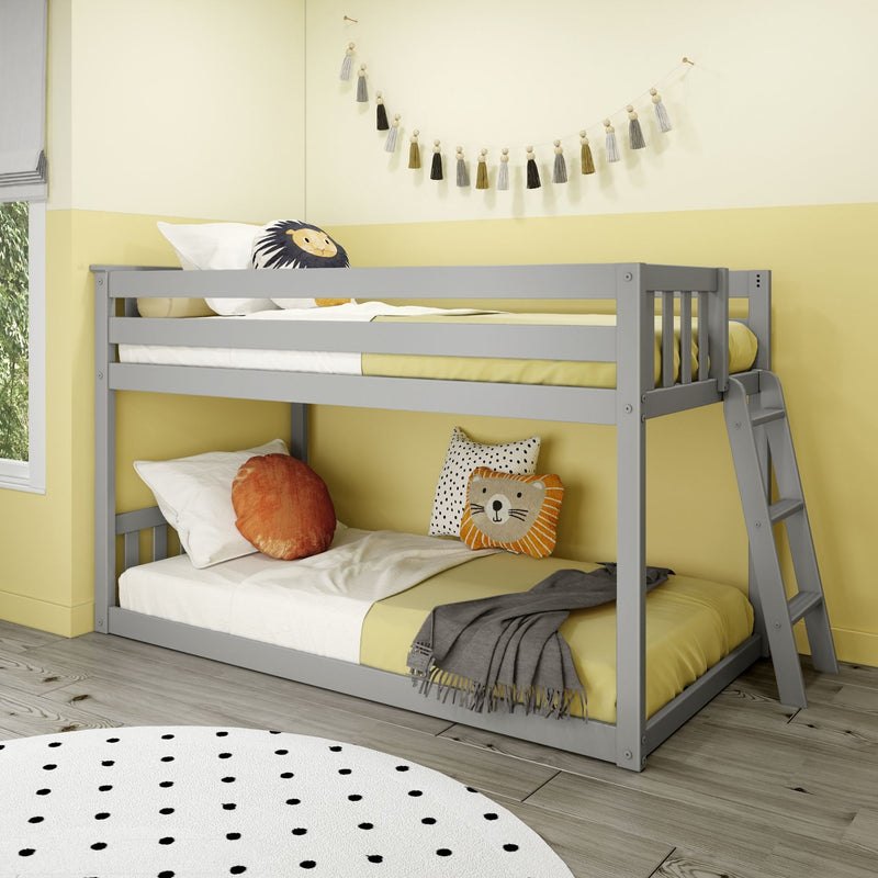 Gray wooden bunk bed in a modern children's bedroom with yellow bedding, decorative tassel garland, lion throw pillow, polka-dot rug and ladder on light wood floor