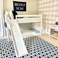 White kids bunk bed with slide in nautical nursery, navy "Don't Give Up The Ship" wall banner, blue geometric rug and neutral plaid accent wall