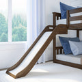 Wooden kids loft bunk bed with slide, blue pillows and white curtains by sunlit window overlooking trees — children's bedroom furniture