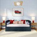 Navy upholstered daybed with red and pink throw pillows against blue-and-white striped wallpaper, framed red vintage SUV wall art, wooden nightstands and lamps