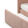 Close-up of blush pink upholstered platform bed corner and headboard with white quilted mattress topper