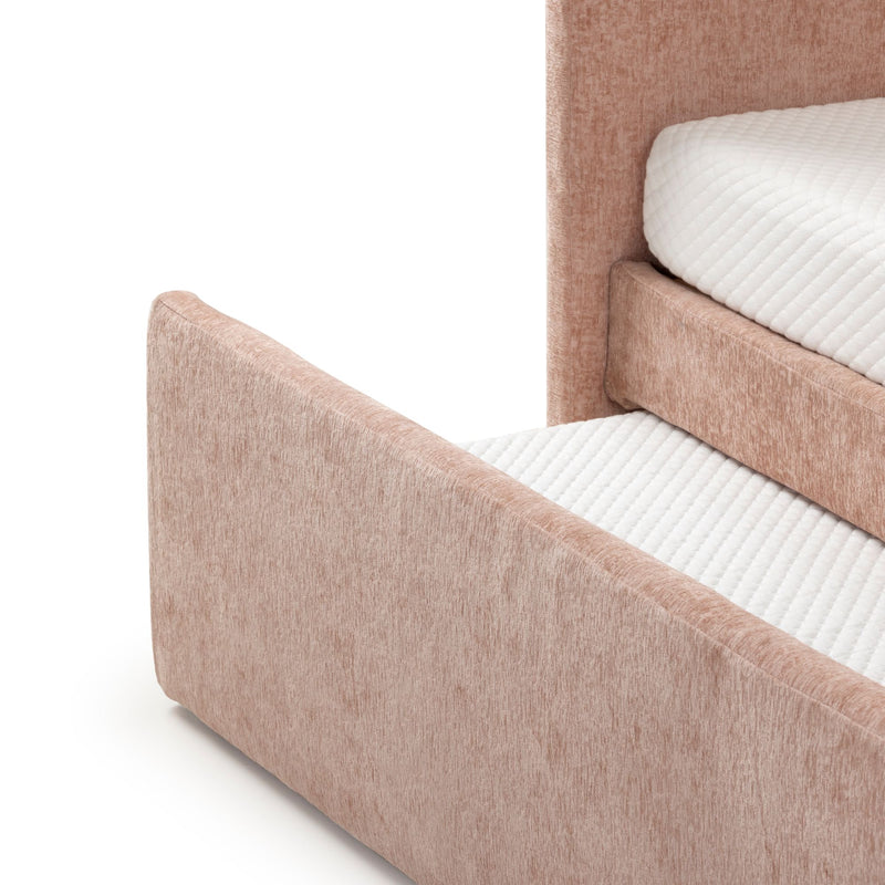 Close-up of blush pink upholstered platform bed corner and headboard with white quilted mattress topper