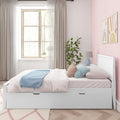 Pastel pink kids bedroom with white storage daybed, pastel bedding and pillows, blue throw, beige curtains, potted plant and sun-and-rainbow wall art in soft natural light