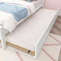 White twin trundle bed with pull-out mattress, pink scallop wallpaper and pastel bedding topped by a blue throw in girls' bedroom
