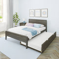 Grey wood platform bed with pull-out trundle, white quilt and pastel pillows, bedside table with lamp, potted plant and framed nursery art on a light blue patterned wall in a bright modern kids' bedroom