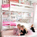 Pink floral girls' bedroom with white bunk bed, plush pink blankets, heart-print pillows and two children reading a book