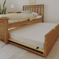 Natural wood trundle bed with pull-out mattress in minimalist bedroom, yellow throw blanket, patterned pillow, bedside lamp and alarm clock