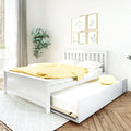 White wooden bed with pull-out trundle and yellow polka-dot duvet in a minimalist bedroom with botanical wall art, fiddle-leaf plant and natural light