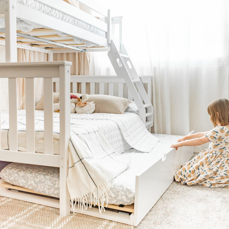 White wooden bunk bed with ladder and pull-out trundle, neutral bedding and plush toys in a bright modern kids' bedroom