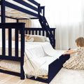 Navy blue wooden bunk bed with pull-out trundle and ladder, white quilted bedding and decorative pillows with plush toys in a bright, space-saving kids' bedroom