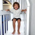 Smiling child with curly hair sitting on a white bunk bed in a bright kids' bedroom, playful family lifestyle and children's bedroom decor