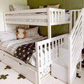 White wooden bunk bed with staircase and trundle drawer in kids' bedroom, plaid bedding, fox plush toy and green accent wall