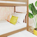 Wooden bunk bed with white bedding and yellow accent pillow in a pastel geometric kids' bedroom with tropical plant