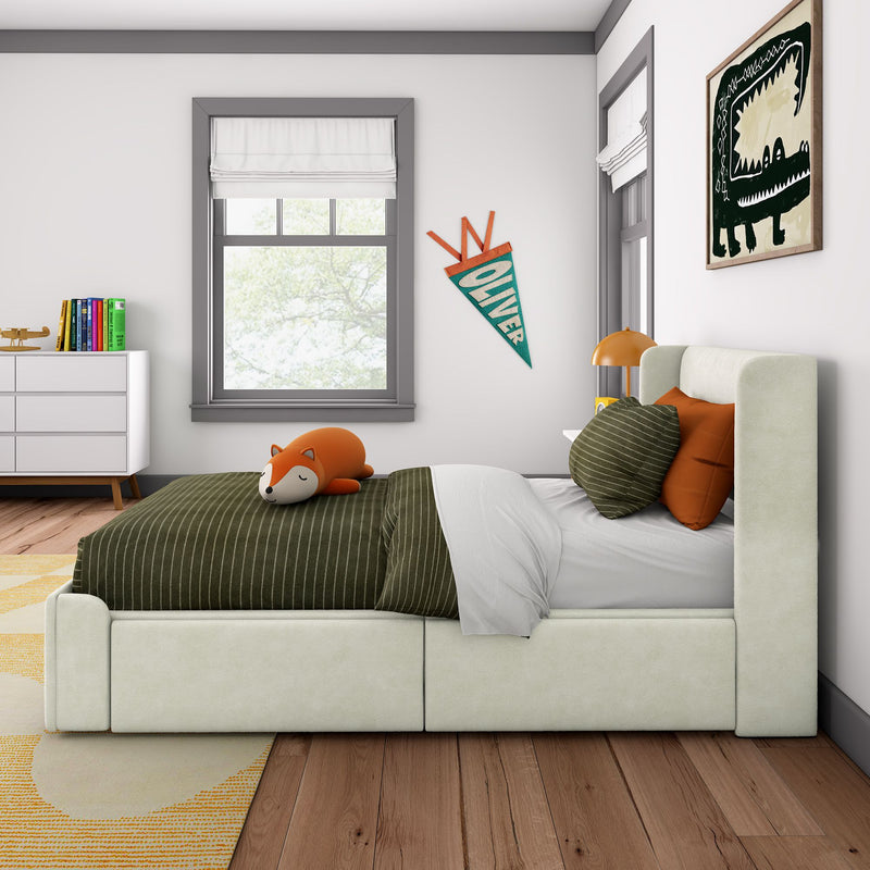 Modern kids bedroom with a stuffed fox on green striped bedding, cream upholstered bed, orange accent pillows, "Oliver" pennant on wall, abstract dinosaur artwork, white dresser with colorful books and gray-trimmed windows