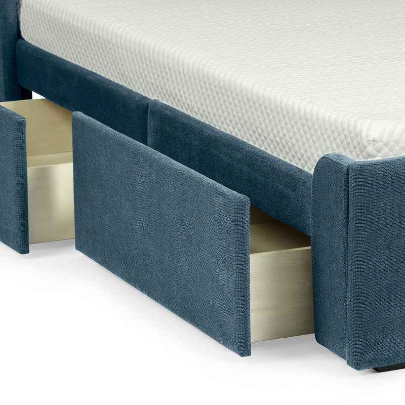 Close-up of a modern upholstered storage bed: blue fabric frame with open under-bed drawers and a white quilted mattress.